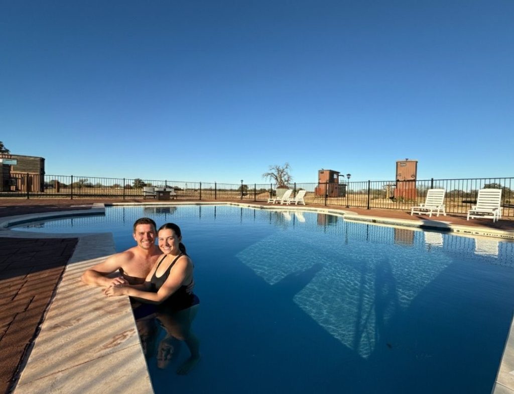 A couple enjoying dinner and drinks at a fire pit table on a rooftop deck during sunset.
