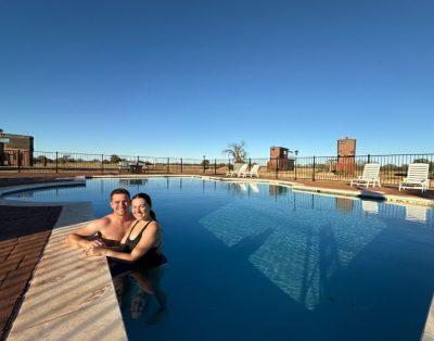 A couple enjoying dinner and drinks at a fire pit table on a rooftop deck during sunset.